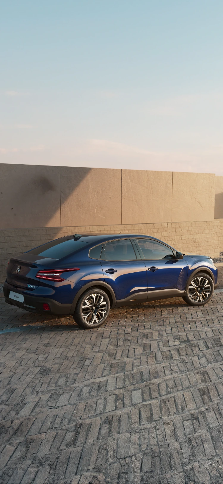 Vue latérale de la Citroën C4 X roulant le long de la côte au coucher du soleil, mettant en valeur son profil épuré.