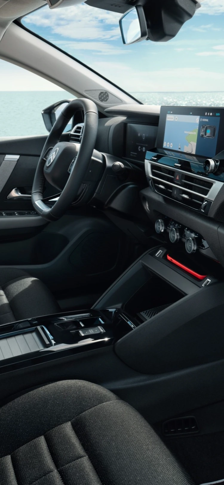 Intérieur avant de la Citroën C4 X, avec le tableau de bord et les sièges mis en valeur sur fond de bord de mer.
