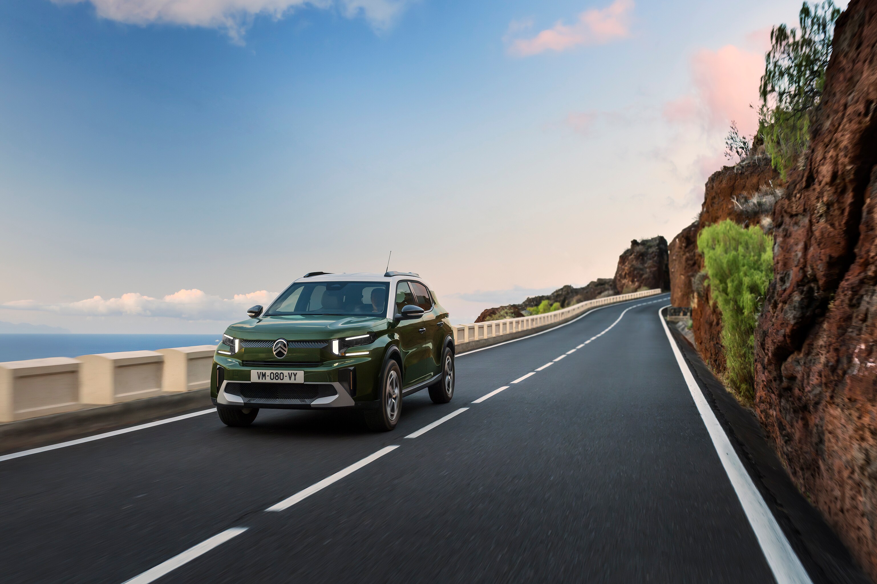 Vue 3/4 avant de Citroën ë-C3 en mouvement sur une route panoramique, une mobilité agile, sûre et abordable.