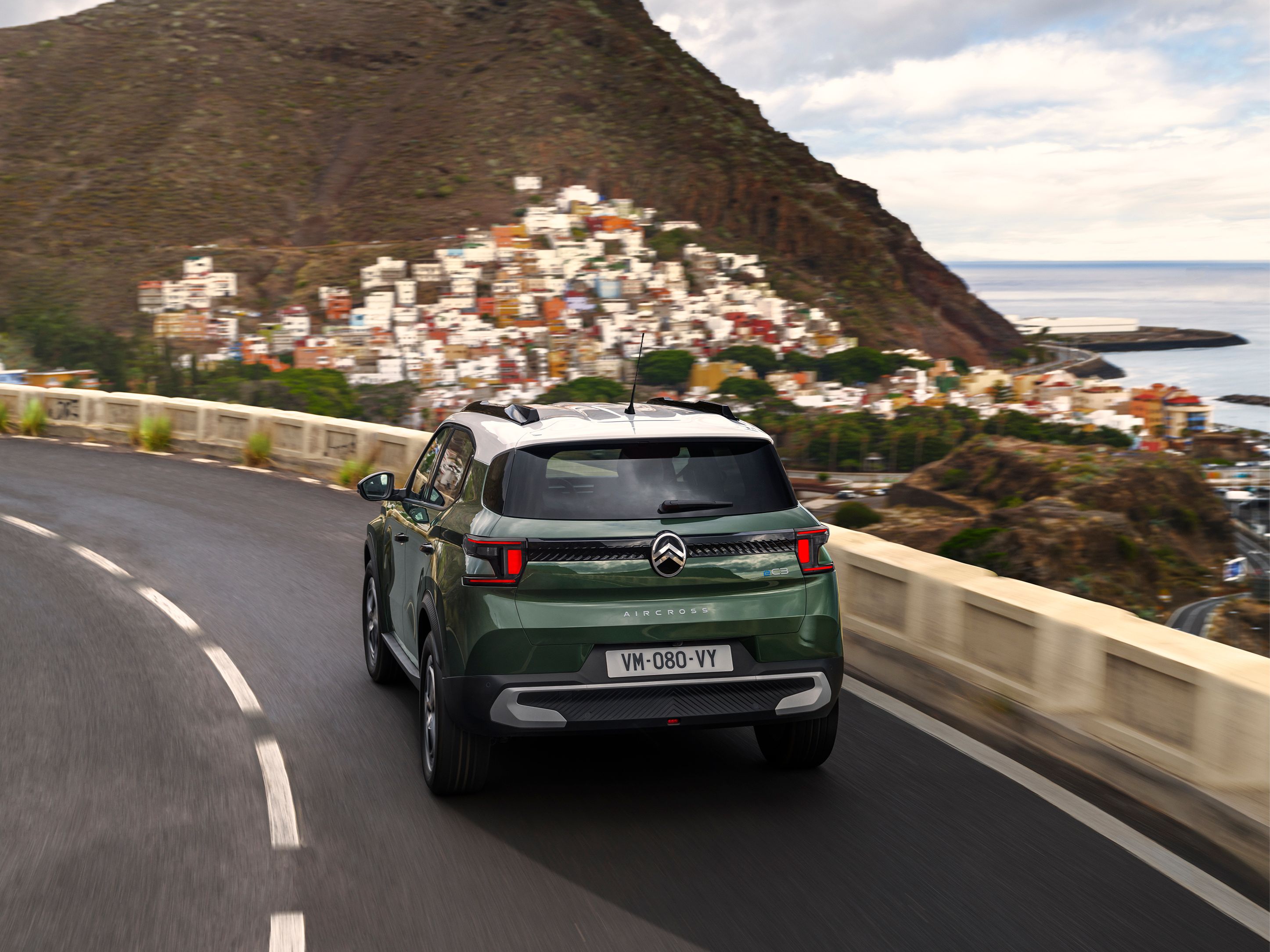 Vue 3/4 arrière de Citroën ë-C3 Aircross sur une route côtière, pour une mobilité sûre, fluide, abordable.
