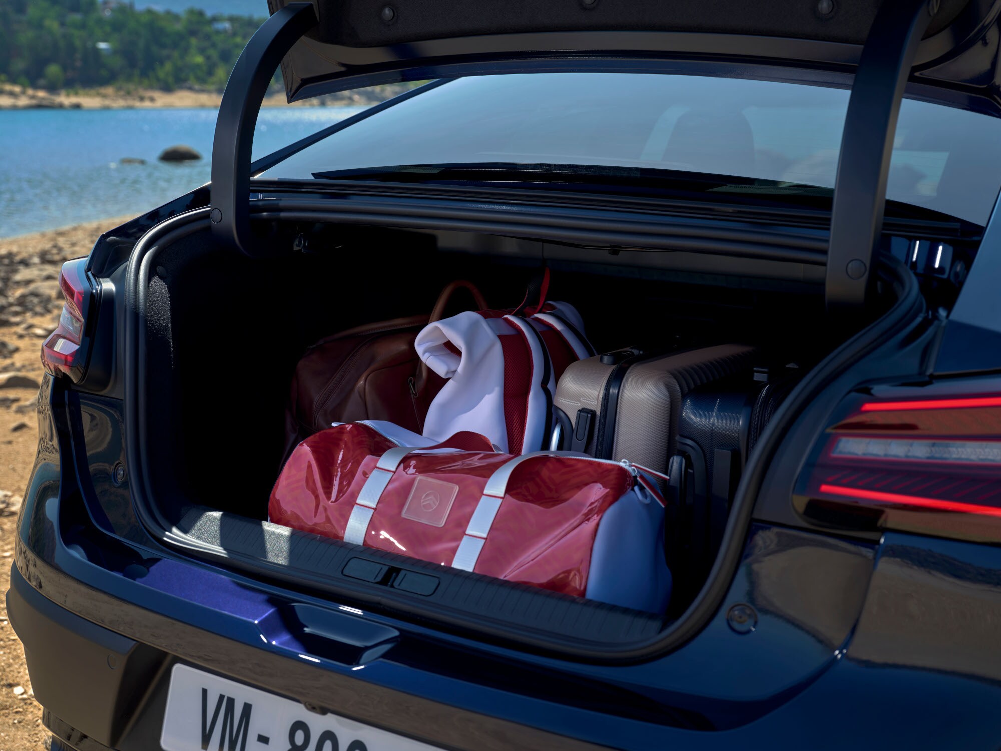 Coffre ouvert de la Citroën C4 X chargé de sacs de voyage au bord d'un lac