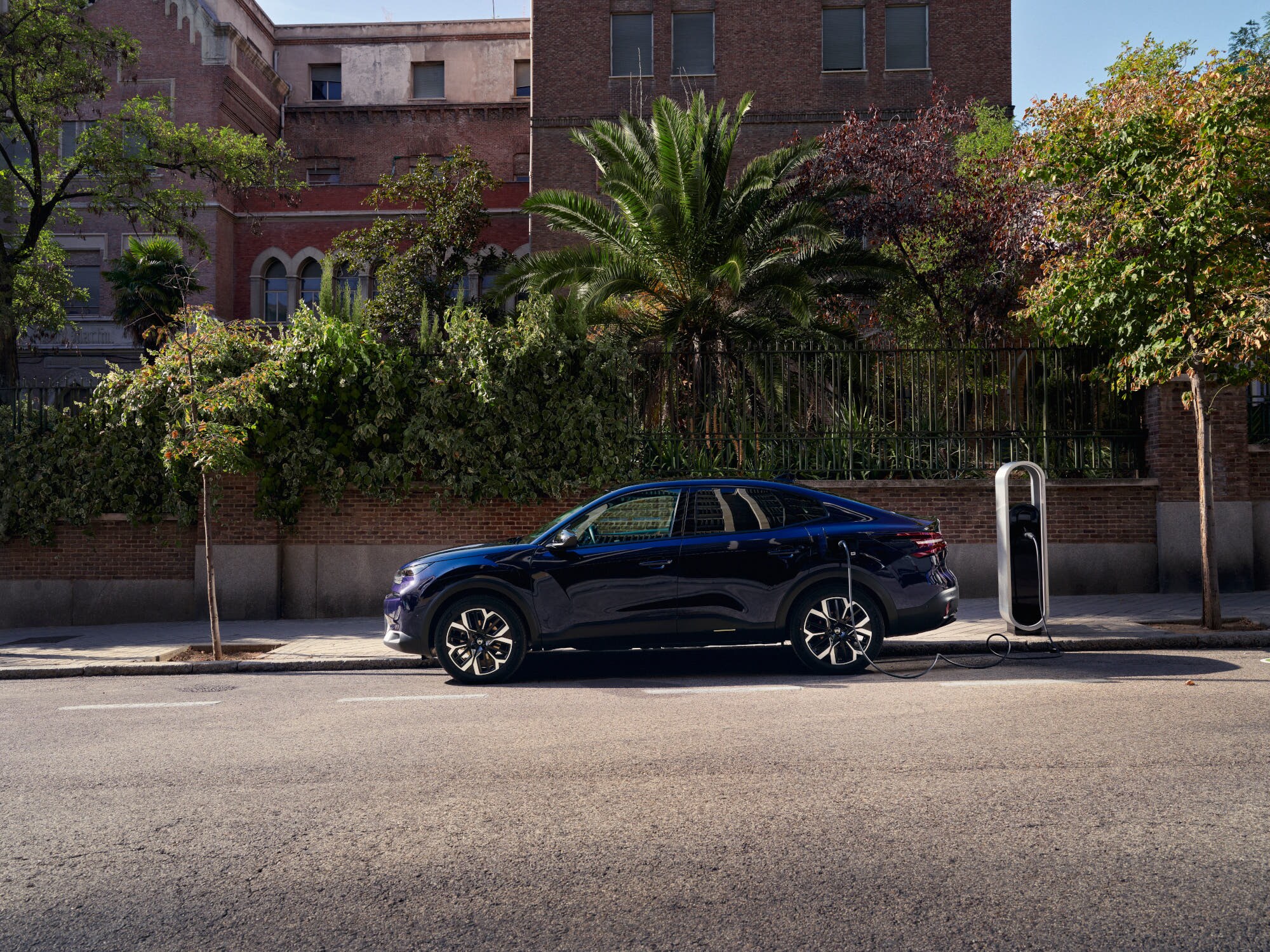 Vue côté de la Citroën C4 X fastback en cours de recharge dans la rue, avec une mobilité urbaine pratique et abordable.